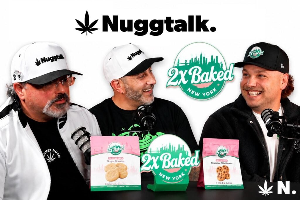 Three people wearing branded hats sit behind microphones during a podcast recording, with 2X Baked logos and packaged cookie products displayed on a table.
